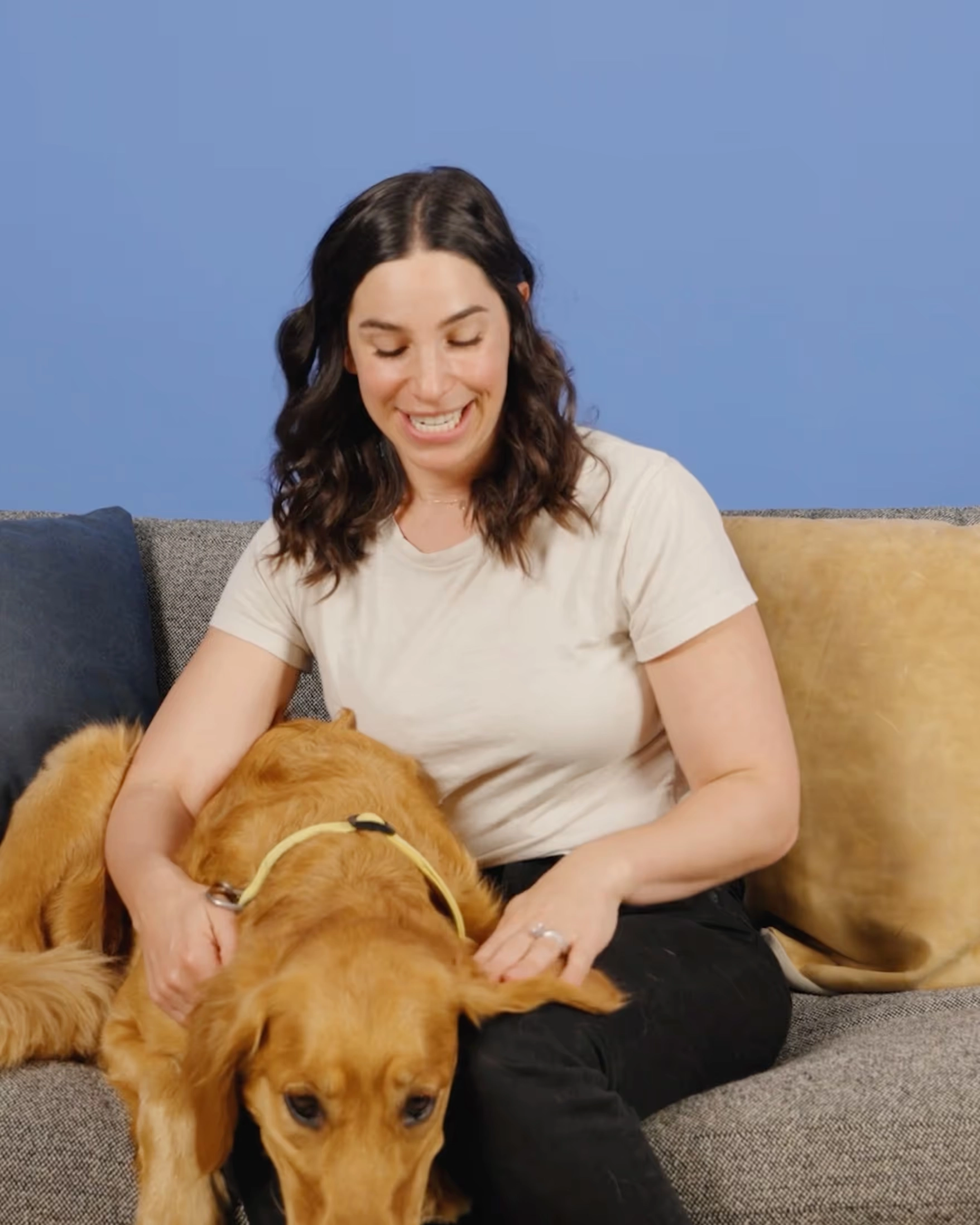 A woman laughing with a golden dog on a sofa