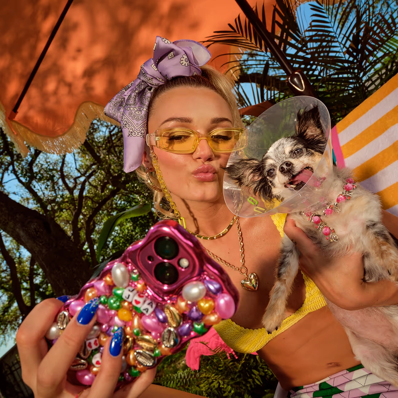 A woman taking a selfie with two small dogs, wearing colorful sunglasses and a head scarf