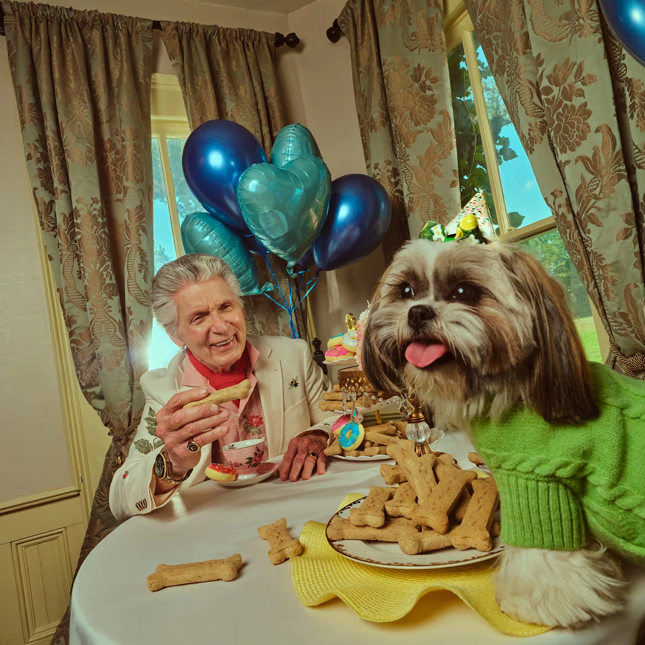 An older woman and a small dog at a birthday table with balloons