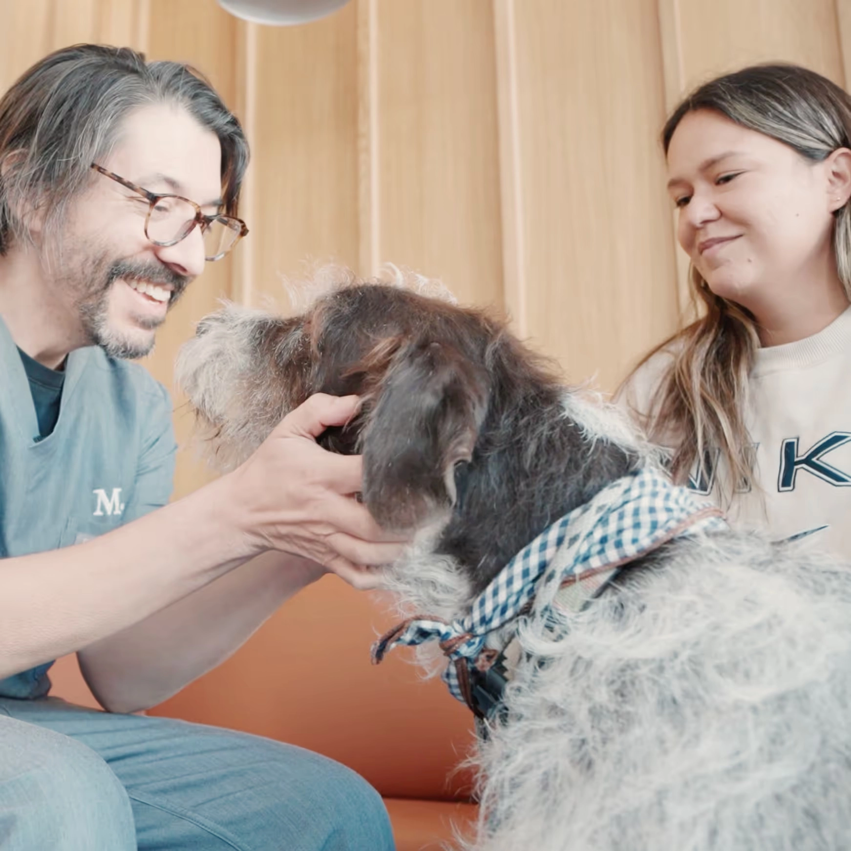 A veterinarian and Natalia smiling over Gunner, a shaggy dog in a blue bandana